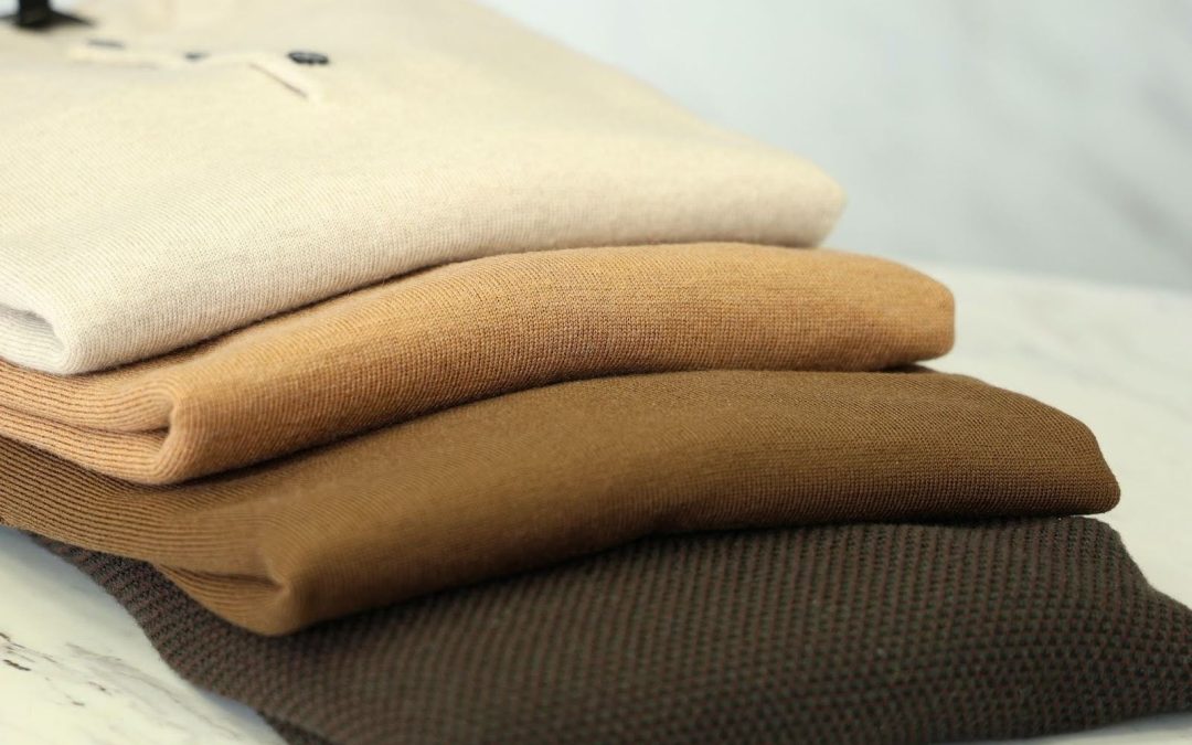 Stack of neatly folded neutral-tone sweaters in beige, tan, and brown hues displayed on a marble surface.